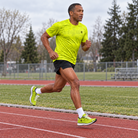 YUL Neon Radioactive Pine men's running shirt, neon yellow, worn by a runner on a track.